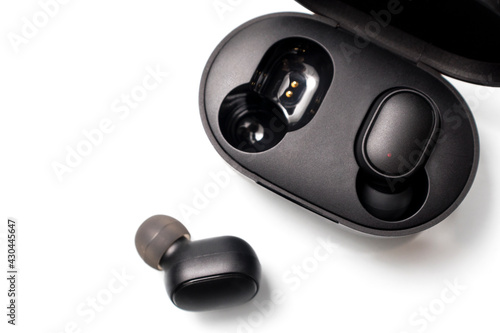 Black wireless bluetooth earphones or headphones, plastic case or box for storage and charging on white background, close up