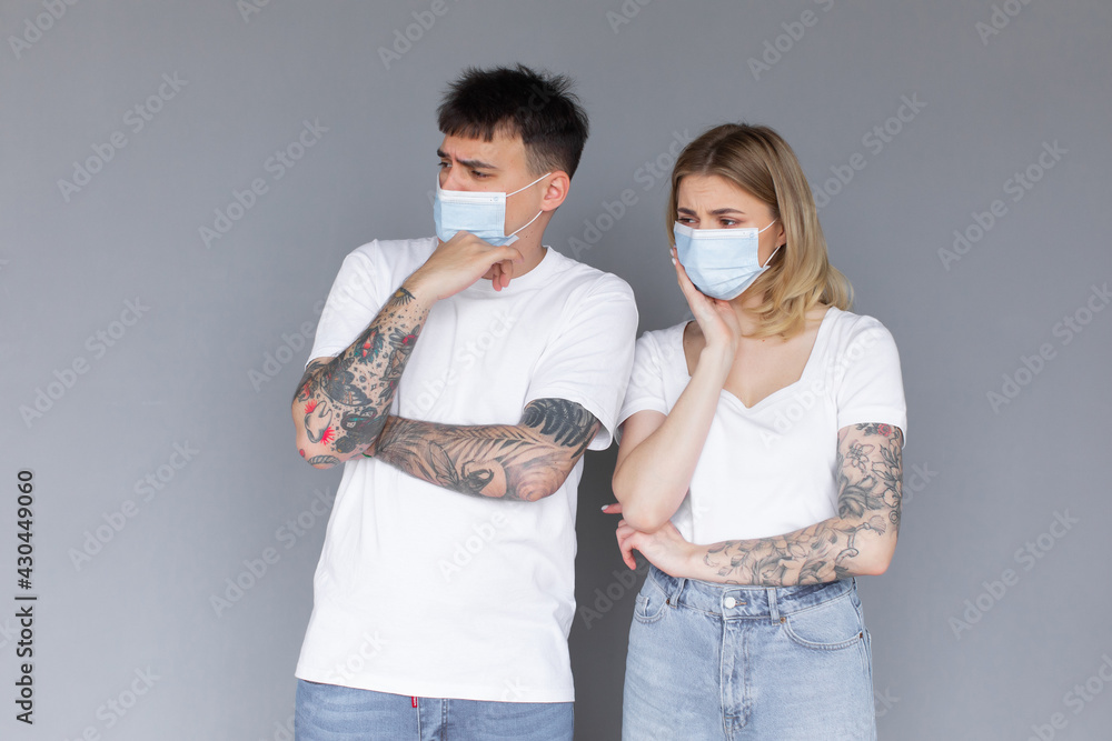 Young excited couple in protective masks isolated over gray background