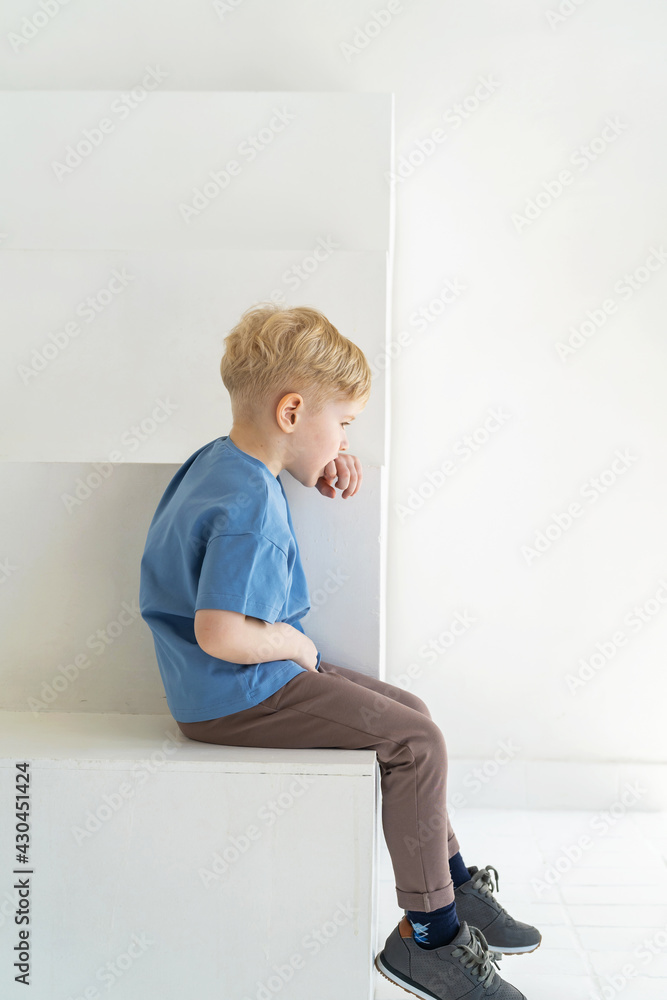 little boy with blond hair, sitting with his back turned away from everyone. The sad child, offended, turned his back. Autism, communication problems, bullying. Full-length little boy with blond hair, sitting with his back turned away from everyone. The sad child, offended, turned his back. Autism, communication problems, bullying. Full-length