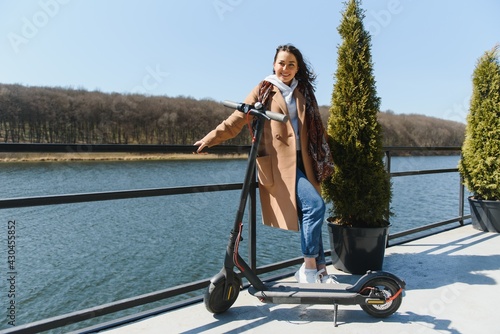 Young beautiful woman riding an electric scooter to work, modern girl, new generation, electric transport, ecology, ecological transport, sunset, electric skateboard. © Serhii