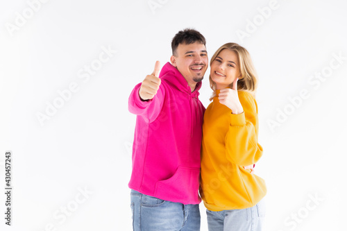 Portrait of excited enthusiastic couple promoters show thumb up recommend choice adverts hug wear color pullover good look isolated over white color background
