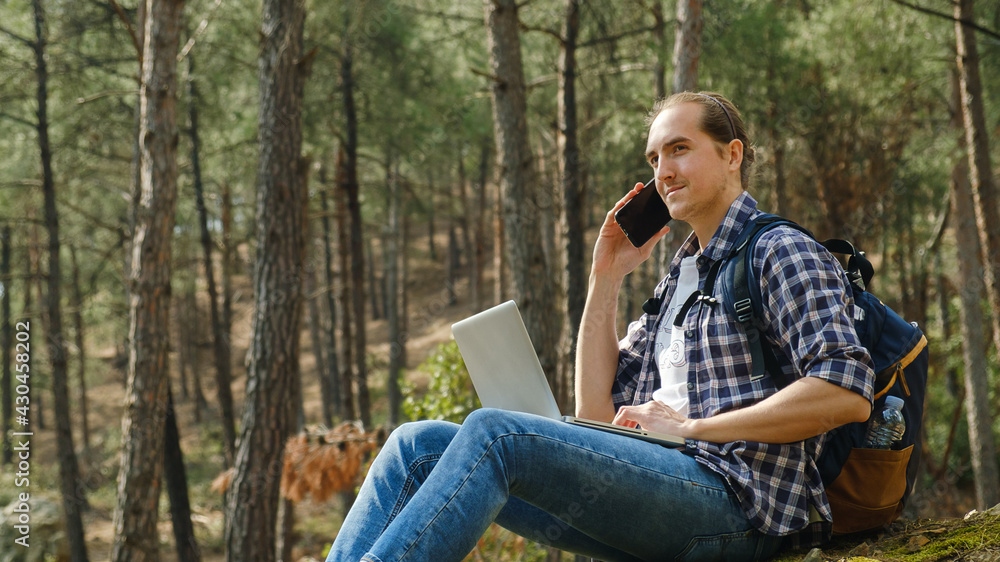 Young man sitting on ground at forest talking on smartphone and working on laptop Young man sitting on ground at forest talking on smartphone and working on laptop