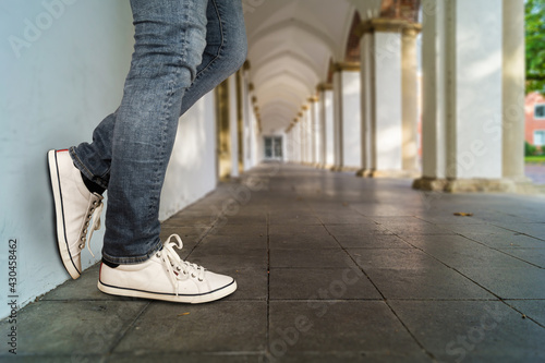 Young fashion man's legs in jeans and white sneaker at a stone wall.