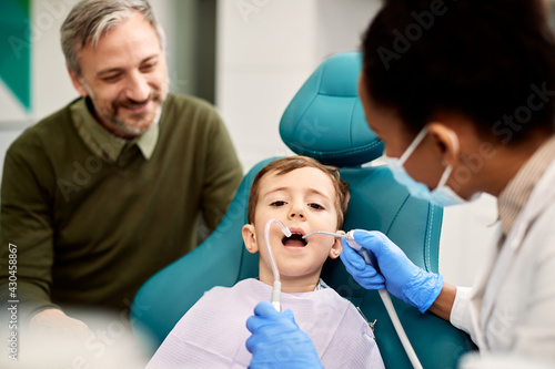 Little boy having dental check-up while being with his father a dentist's office.