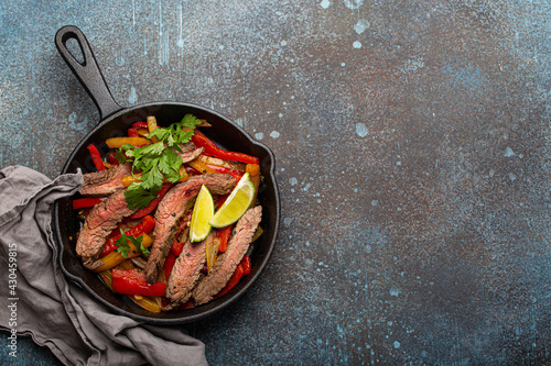 Traditional Mexican dish Beef fajitas with bell peppers in black cast iron pan on rustic stone background from above with space for text, American Mexican food 