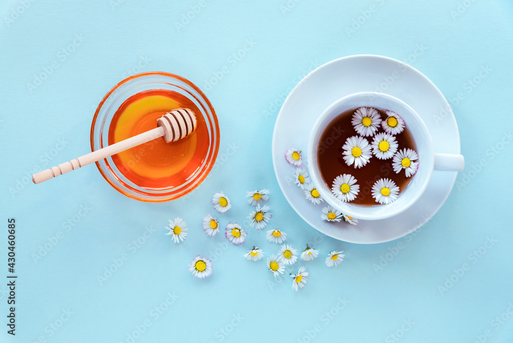 A cup of tea with chamomile and honey in glass bowl with wooden dipper on blue background A cup of tea with chamomile and honey in glass bowl with wooden dipper on blue background