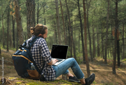 Man sitting on ground at forest talking on smartphone and working on laptop photo