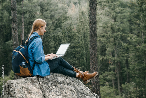 Young woman sitting on ground at forest and working on laptop .