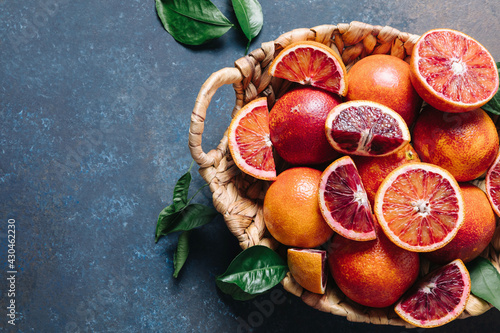 Whole and sliced blood oranges in a basket on blue table background. Flat lay, top view, copy space.