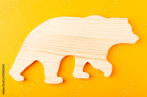 A figurine of a bear carved from solid pine by a hand jigsaw. On a yellow background