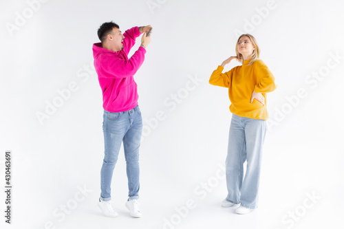 Image of a man take photo of his positive optimistic woman on white background by mobile phone.