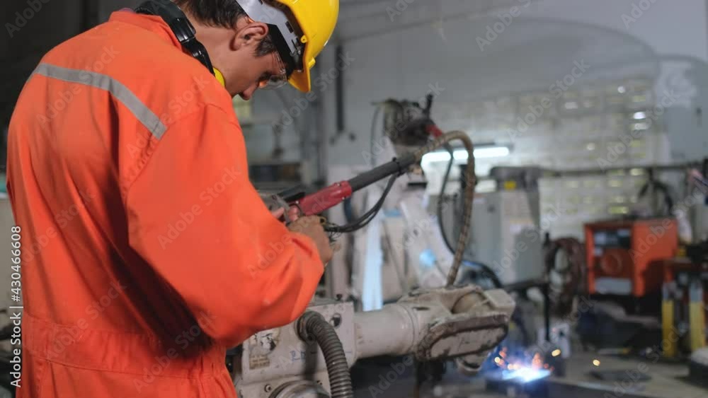 Factory worker man use tool to fix and maintenance part of robotic machine while other machine is working with welding the metal. Factory worker man use tool to fix and maintenance part of robotic machine while other machine is working with welding the metal.