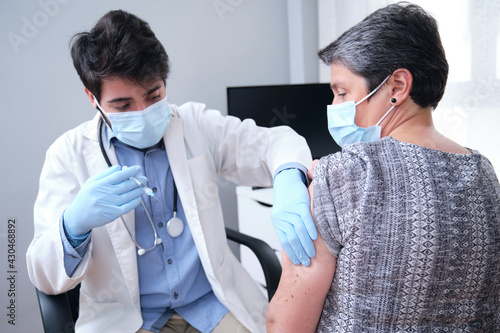 Doctor vaccinating mature woman patient in clinic. Nurse holding syringe before inject Covid-19 or coronavirus vaccine.