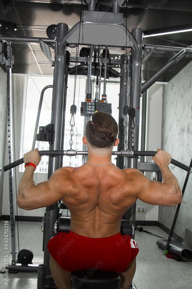 Fototapeta premium a man with big muscles is engaged in weightlifting in the gym. A pumped-up athlete goes in for sports on heavy weight simulators. sport exercises