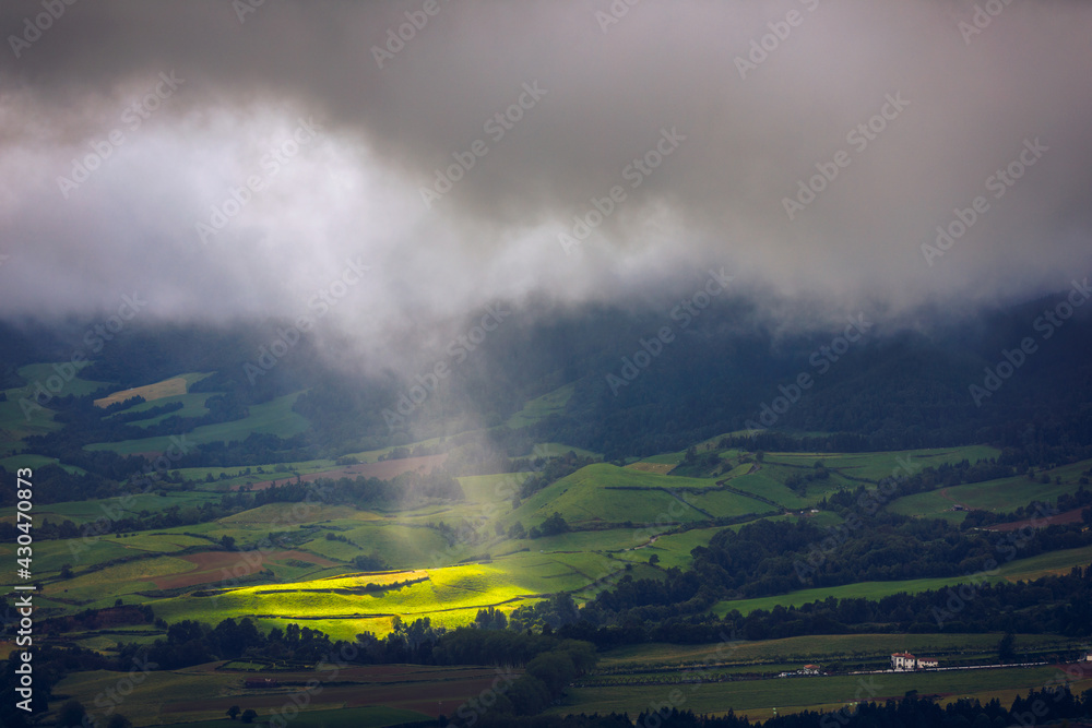Bright sunlight shining through hole of clouds to dark scene of mountain range, Azores, Sao Miguel, Portugal. The beam of light through the dark clouds on the mountains in Azores, Portugal.