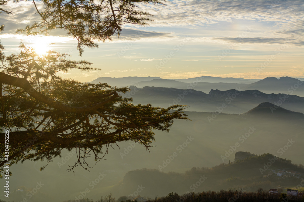 Panorama pomeridiano, con sole basso e prospettiva di montagne con foschia, visto dalla Repubblica di San Marino