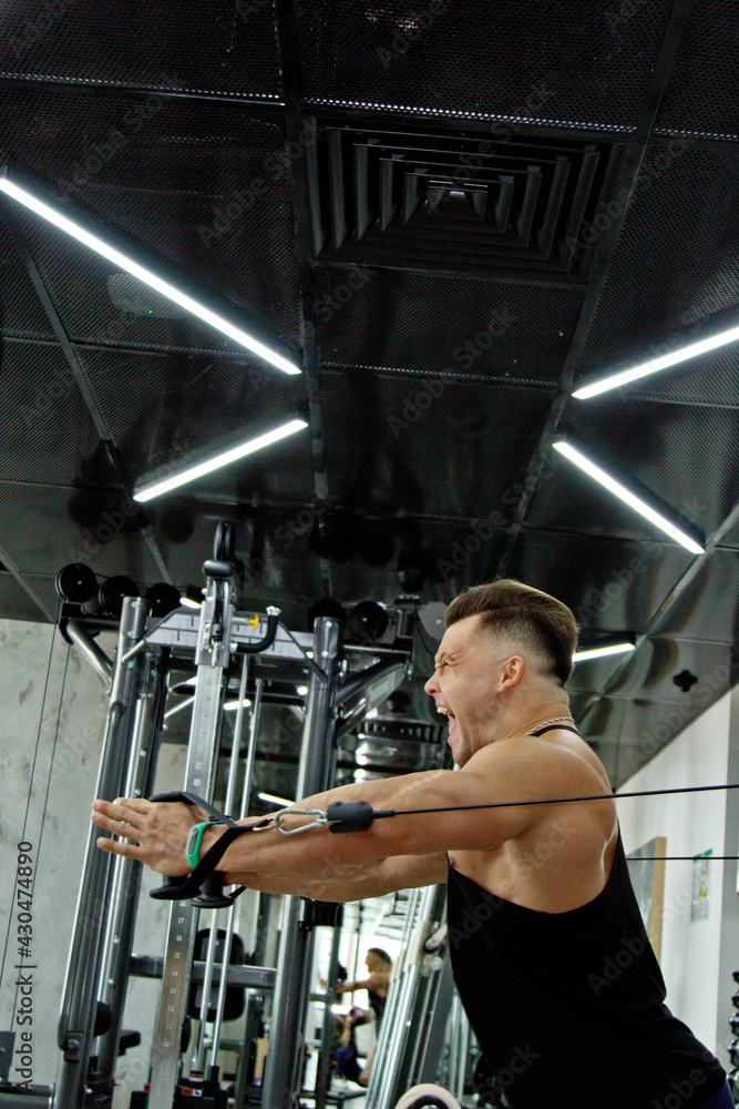 a man with big muscles is engaged in weightlifting in the gym. A pumped-up athlete goes in for sports on heavy weight simulators. sport exercises. Vivid emotions of work on the face a man with big muscles is engaged in weightlifting in the gym. A pumped-up athlete goes in for sports on heavy weight simulators. sport exercises. Vivid emotions of work on the face