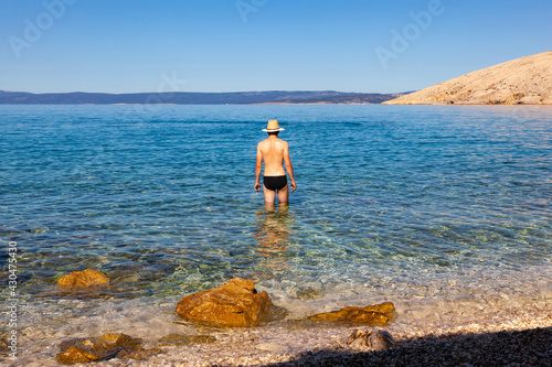 Young man with straw hat in the sea water on beach during the summer vacation, Stara Baska. krk