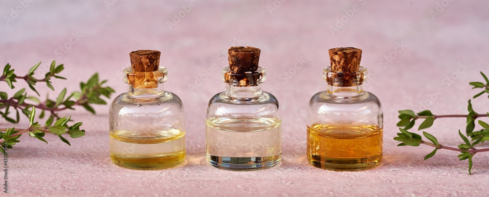 Essential oil bottles with fresh thyme twigs on pastel pink background Essential oil bottles with fresh thyme twigs on pastel pink background