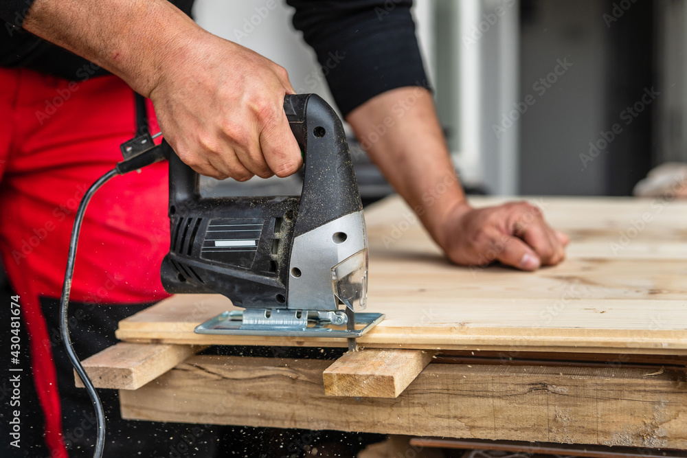 Close up on hand of unknown carpenter working with an electric jigsaw cutting wood with saw woodworking hobby concept copy space