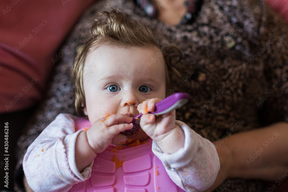 Portrait of a little blond toddler girl. Spoon eating. Dirty mouth. Mom feeds the baby. Portrait of a little blond toddler girl. Spoon eating. Dirty mouth. Mom feeds the baby.