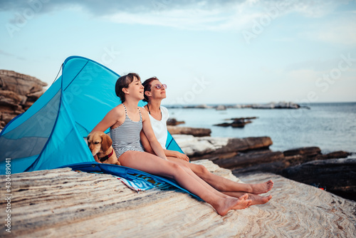 Mother and daughter looking into sunset while sitting in beach tent with dog © kerkezz