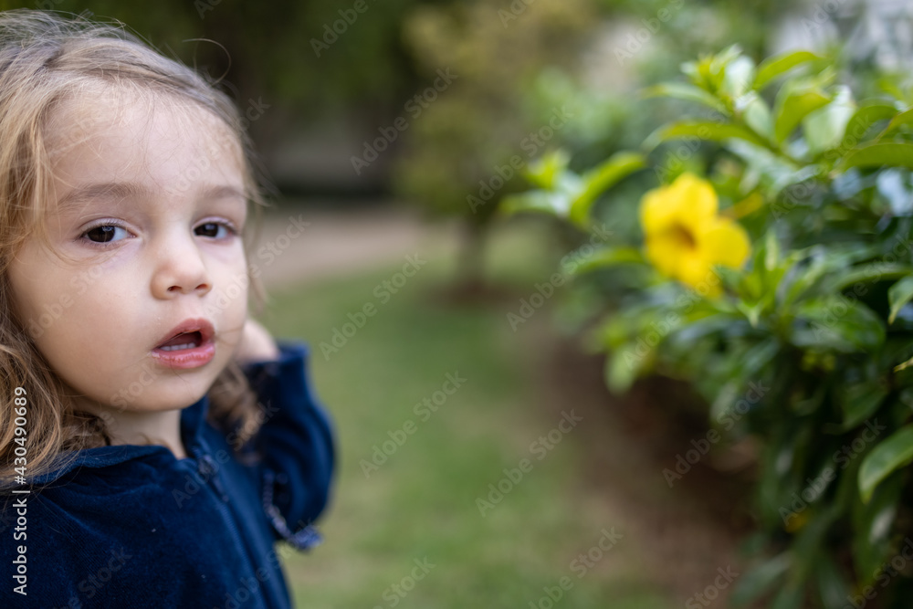 Criança menina loira brincando no jardim com uma flor amarela Criança menina loira brincando no jardim com uma flor amarela