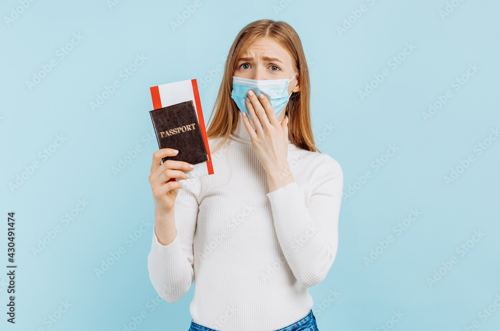 Shocked frightened young woman, in medical mask, holding passport with tickets Shocked frightened young woman, in medical mask, holding passport with tickets