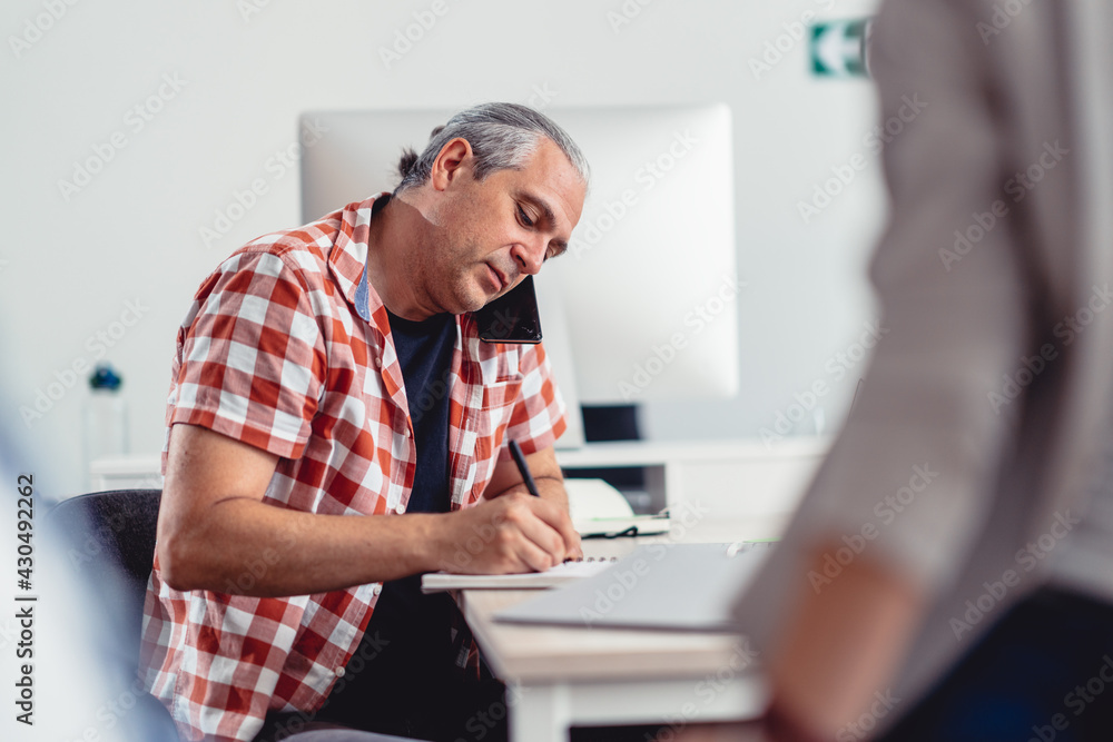 Fototapeta premium Businessman using phone and writing notes in the office