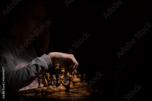girl in the shadows plays vintage chess on a dark background. old chess. business concept