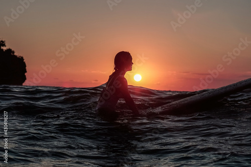 Portrait from the water of surfer girl with beautiful body on surfboard in the ocean at sunset time © Lila Koan