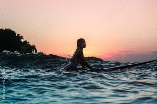 Portrait from the water of surfer girl with beautiful body on surfboard in the ocean at sunset time