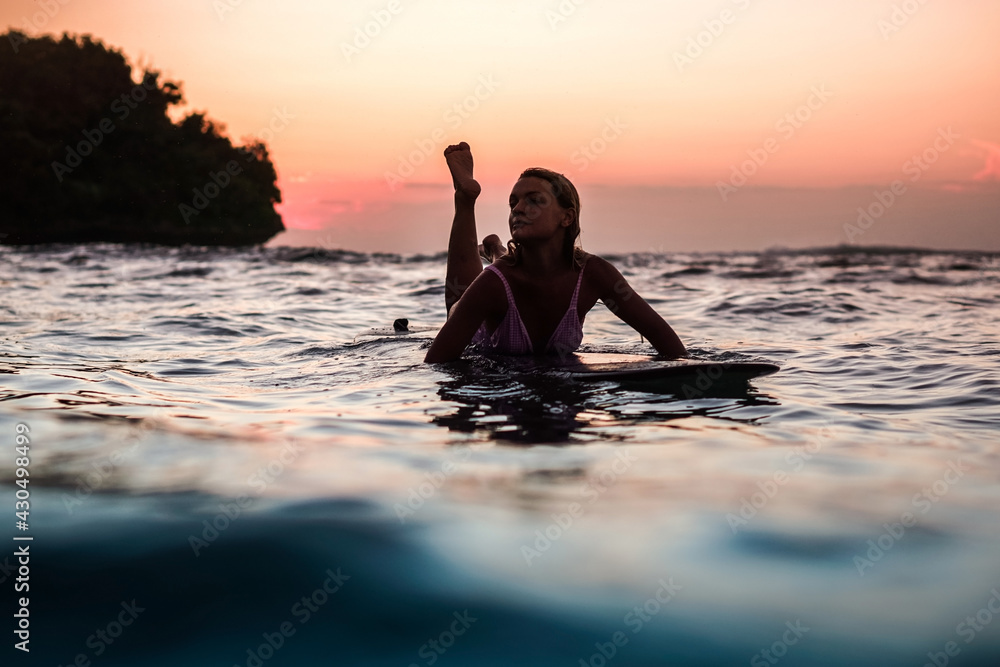 Portrait from the water of surfer girl with beautiful body on surfboard in the ocean at sunset time in Bali