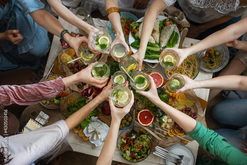 Top view closeup female friends hands cheers toasting glass of healthy beverage over serving table