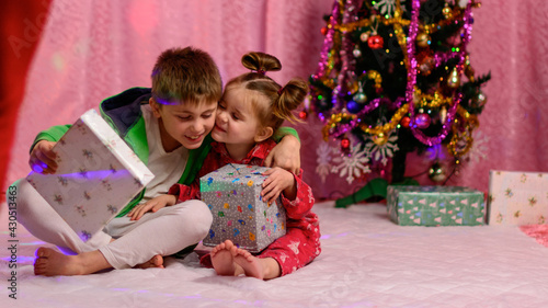 A brother and sister are looking at presents near the Christmas tree on Christmas Eve.