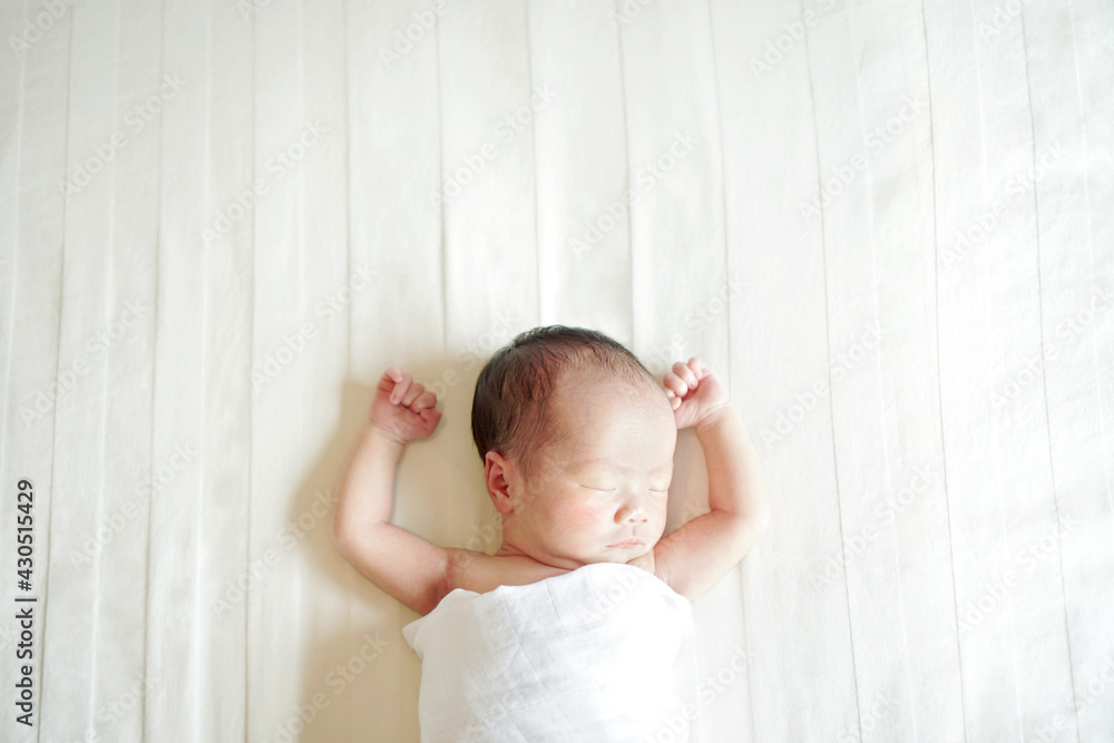 Newborn sleeping with arms up on white linen bed sheet. Top view at cute little baby laying at
