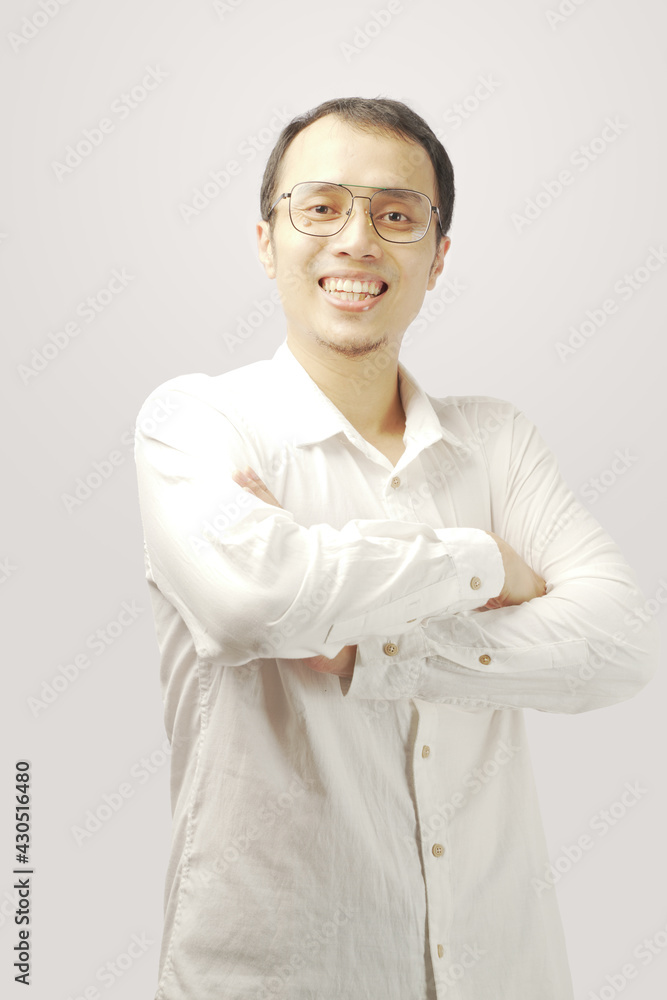 Confident young man in white t-shirt crossing hands on chest and looking at camera while standing against gray background. Confident young man in white t-shirt crossing hands on chest and looking at camera while standing against gray background.