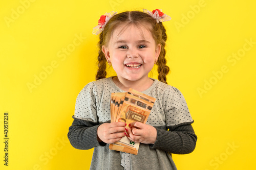 Portrait of a girl on a yellow background, a child holding money in his hands, a large amount of money, the European euro and a child.