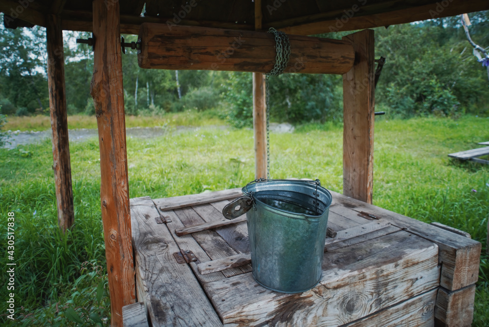 A bucket for water on an old traditional well dug in the ground for the extraction of clean water in the Altai mountains A bucket for water on an old traditional well dug in the ground for the extraction of clean water in the Altai mountains