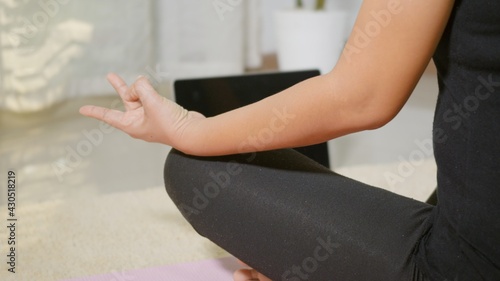 Fototapeta Naklejka Na Ścianę i Meble -  Asian young woman leggings practicing yoga at home sitting in lotus pose on yoga mat for balance, female working out at home in living room. lifestyle sport healthy meditation concept, slow motion