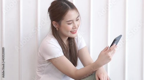Smiling happy beautiful Asian woman relaxing using technology of phone near white wall at home