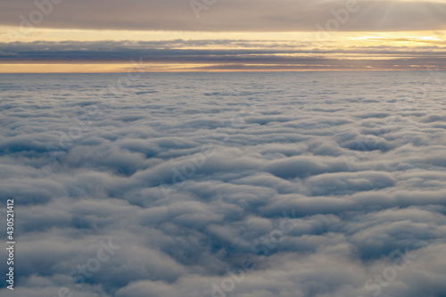 Morning dawn, the sun rises on the horizon, breaking through a light band over white fluffy clouds lying in rounded white dunes, an aerial picture taken from an airplane height of ten thousand meters.