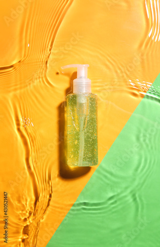 Bottle of cosmetic product in water on color background
