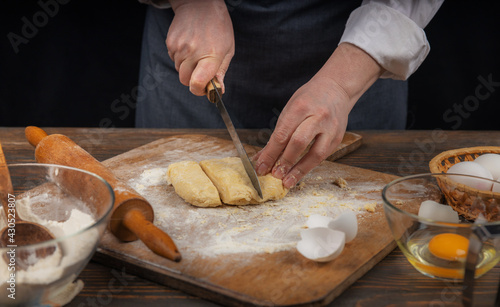 Women's hands, flour and dough. A woman in an apron cooking dough for homemade baking, a rustic home cozy atmosphere, a dark background with unusual lighting.