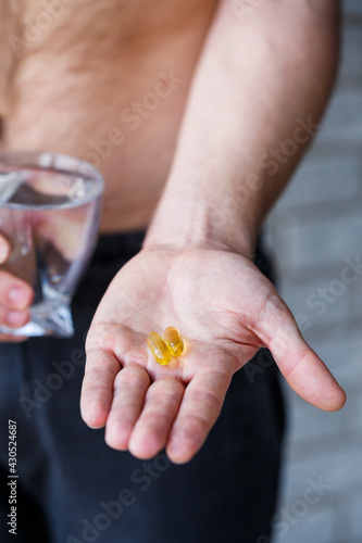A young man holds vitamins and a glass of water in his hands. Immunity pills