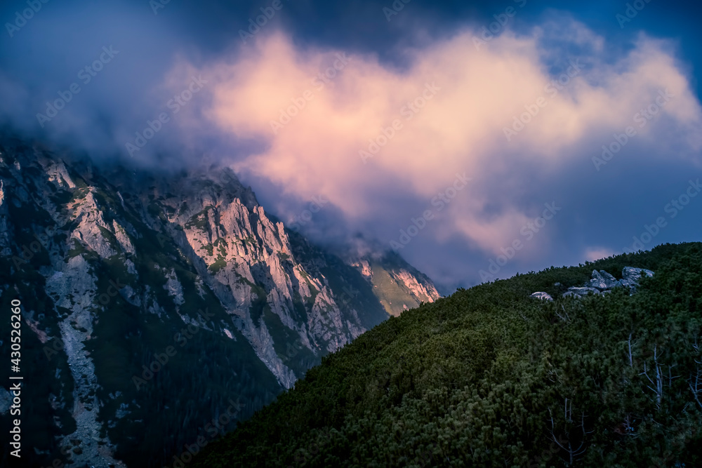 Dramatic sky over Dolina Roztoki Valley, High Tatra Mountains, Poland. Sunset illuminating the clouds and rocky formations. Selective focus on the pine forest, blurred background.