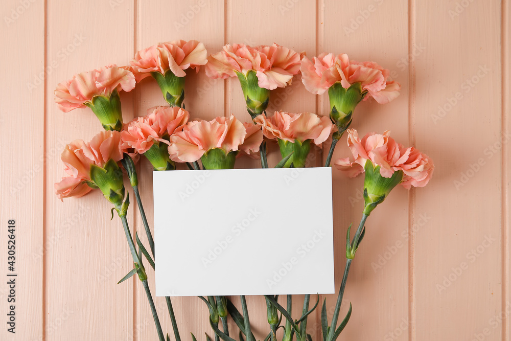 Fototapeta premium Fresh carnation flowers with empty paper sheet on color wooden background