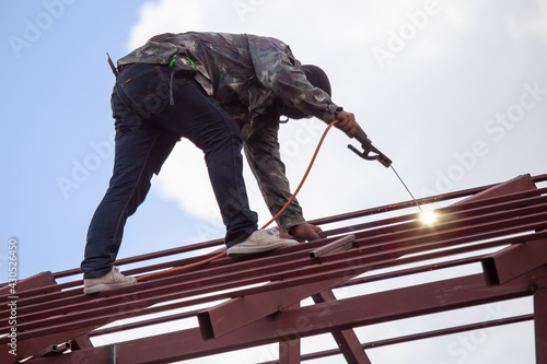 Wallpaper Mural Red painted steel roof truss, with roof welders working at dangerous heights. Welding of steel is very technically demanding and is only professional. Bright sky background Torontodigital.ca