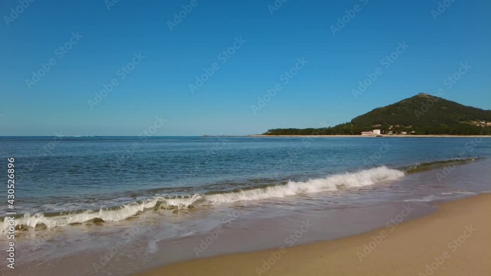 Ocean beach with the green mountain on the background. Calm sea waves. Summer vacation. Spain. Portugal. Caminha. Moledo. Ocean beach with the green mountain on the background. Calm sea waves. Summer vacation. Spain. Portugal. Caminha. Moledo.
