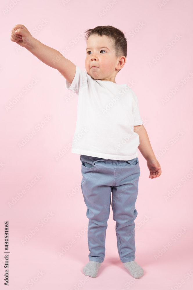 Happy little kid imitate superhero. Boy in a superman pose on pink background Happy little kid imitate superhero. Boy in a superman pose on pink background